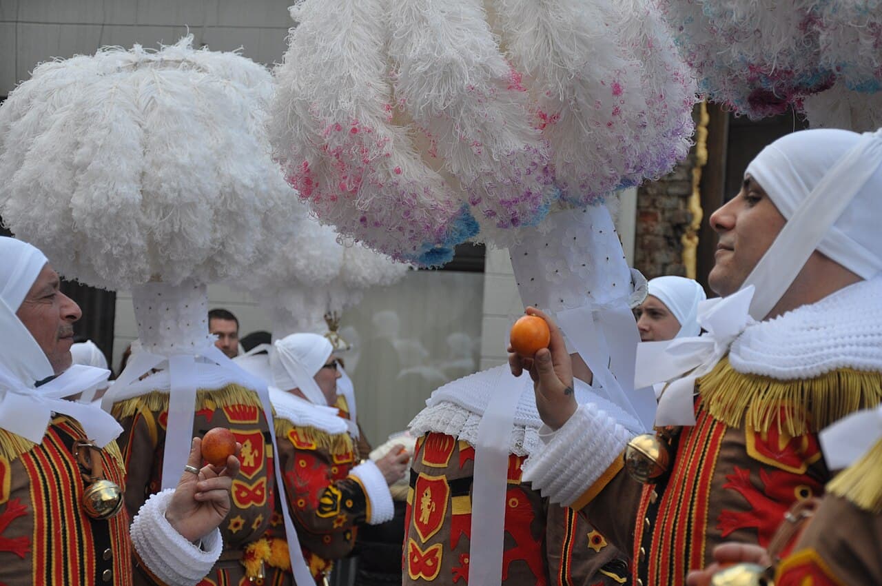 Gilles at the Carnival of Binche holding oranges, wearing tall white ostrich-feather hats