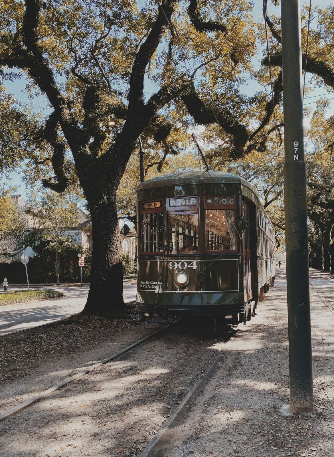 An Uptown-bound St. Charles Avenue streetcar rolling under live oaks in New Orleans