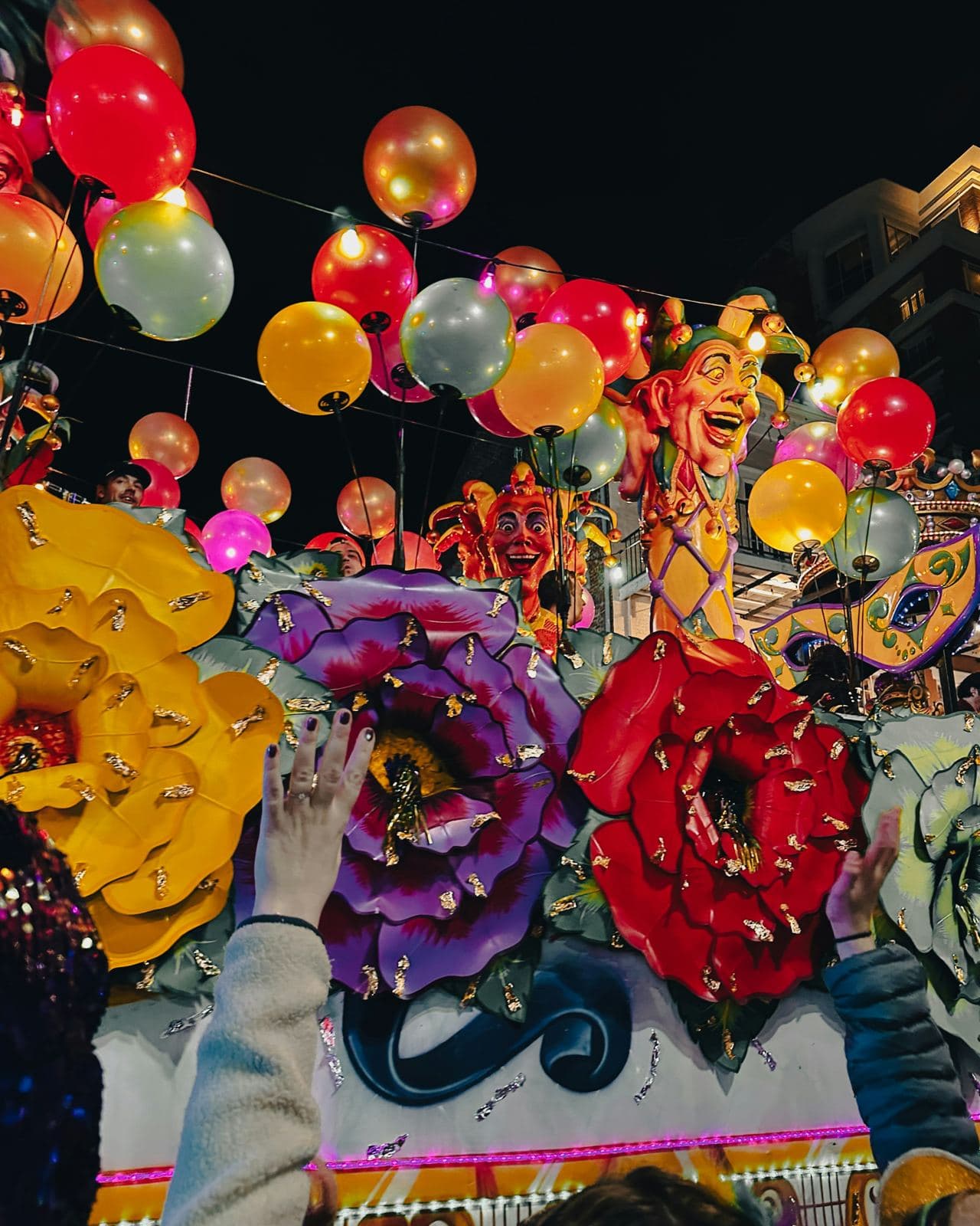 A crowd reaches up toward a colorful Mardi Gras float as riders throw beads during a New Orleans parade