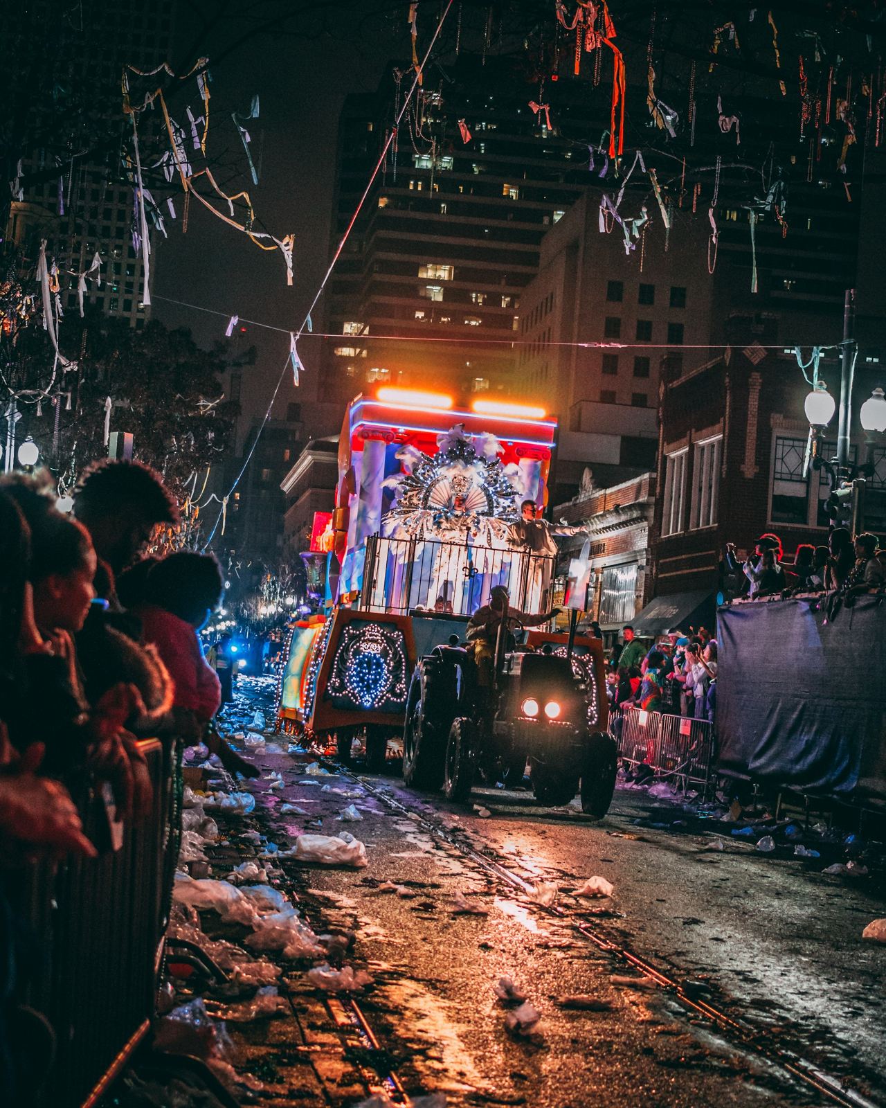 A lit Mardi Gras float rolls between packed crowds on a New Orleans street at night